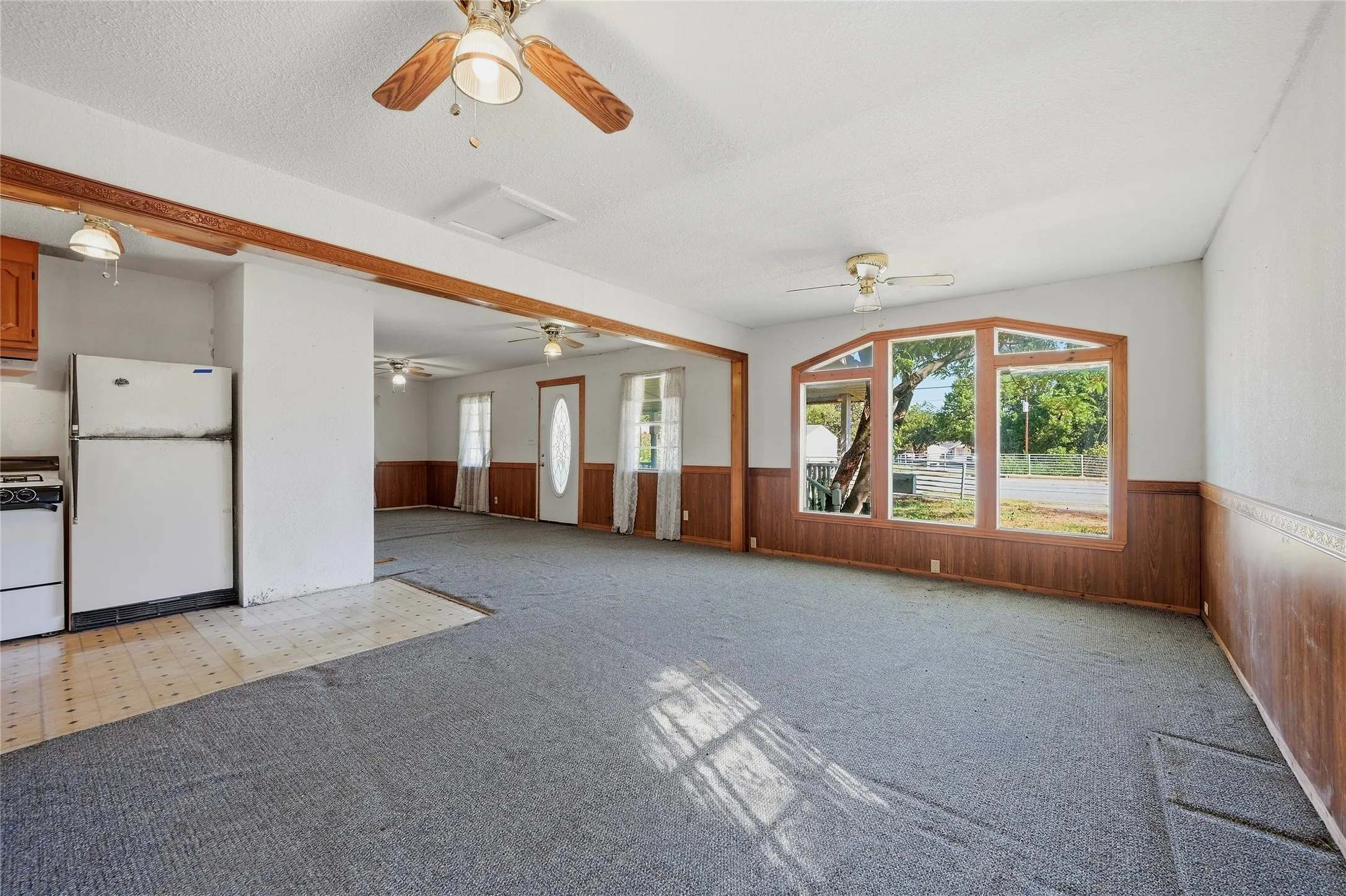 Open-concept interior featuring wood-finish wall panels, bay windows, and ceiling fans