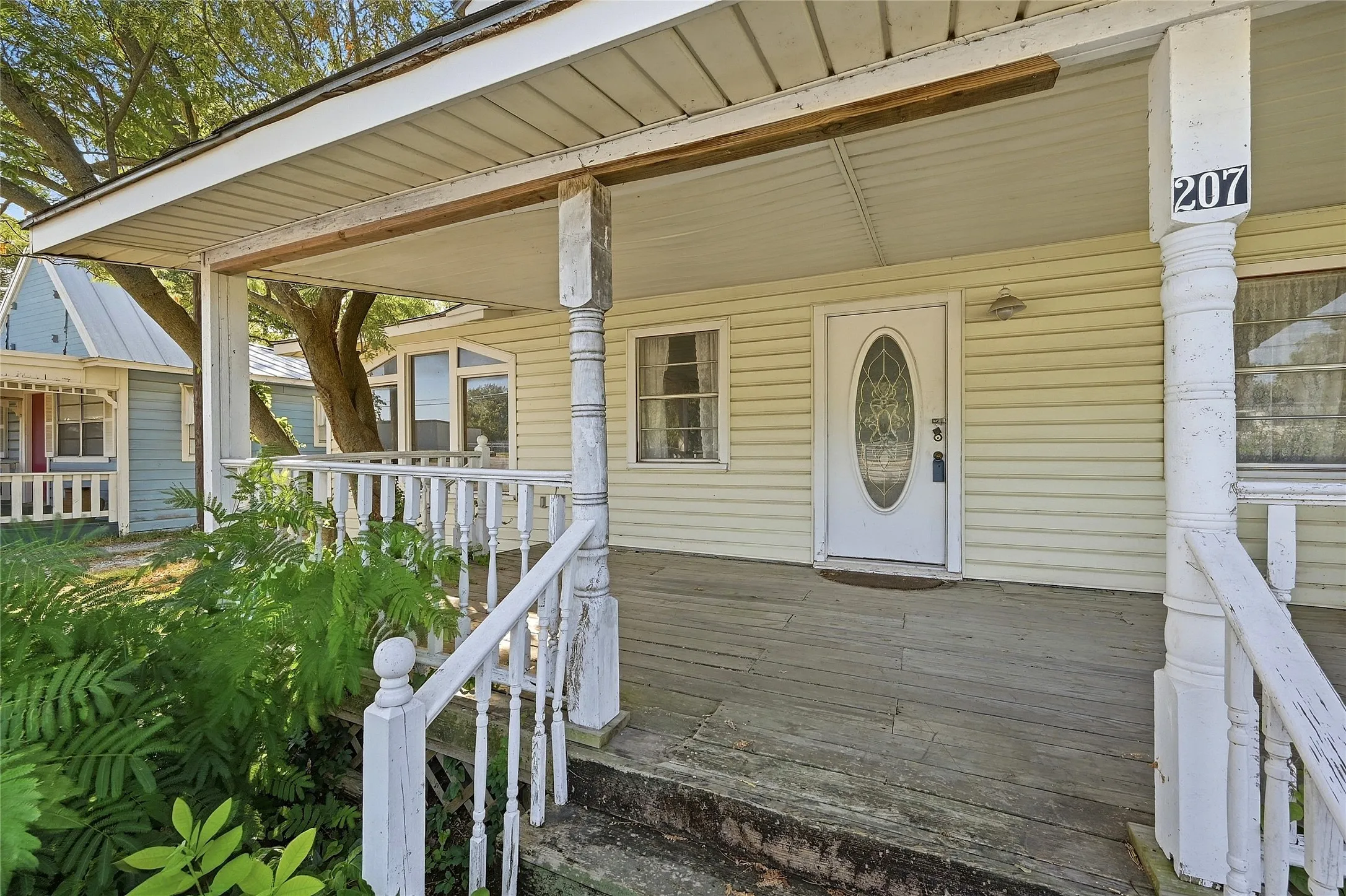 Front porch with white railing and spindles, oval glass front door, house numbering on column, and horizontal siding