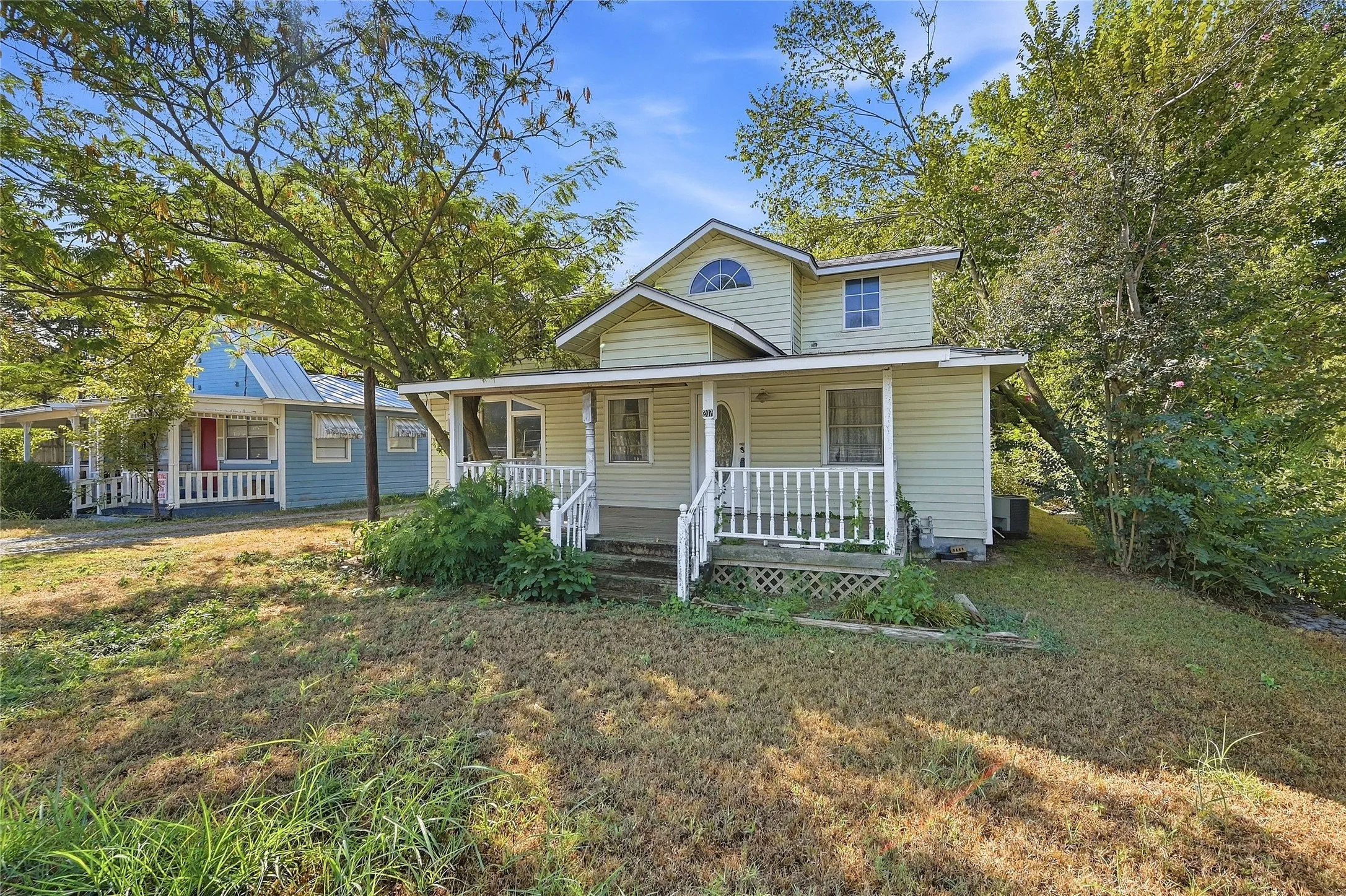 Two-story residence with a covered front porch featuring white railing, light-colored siding, and a decorative arched window on the upper level