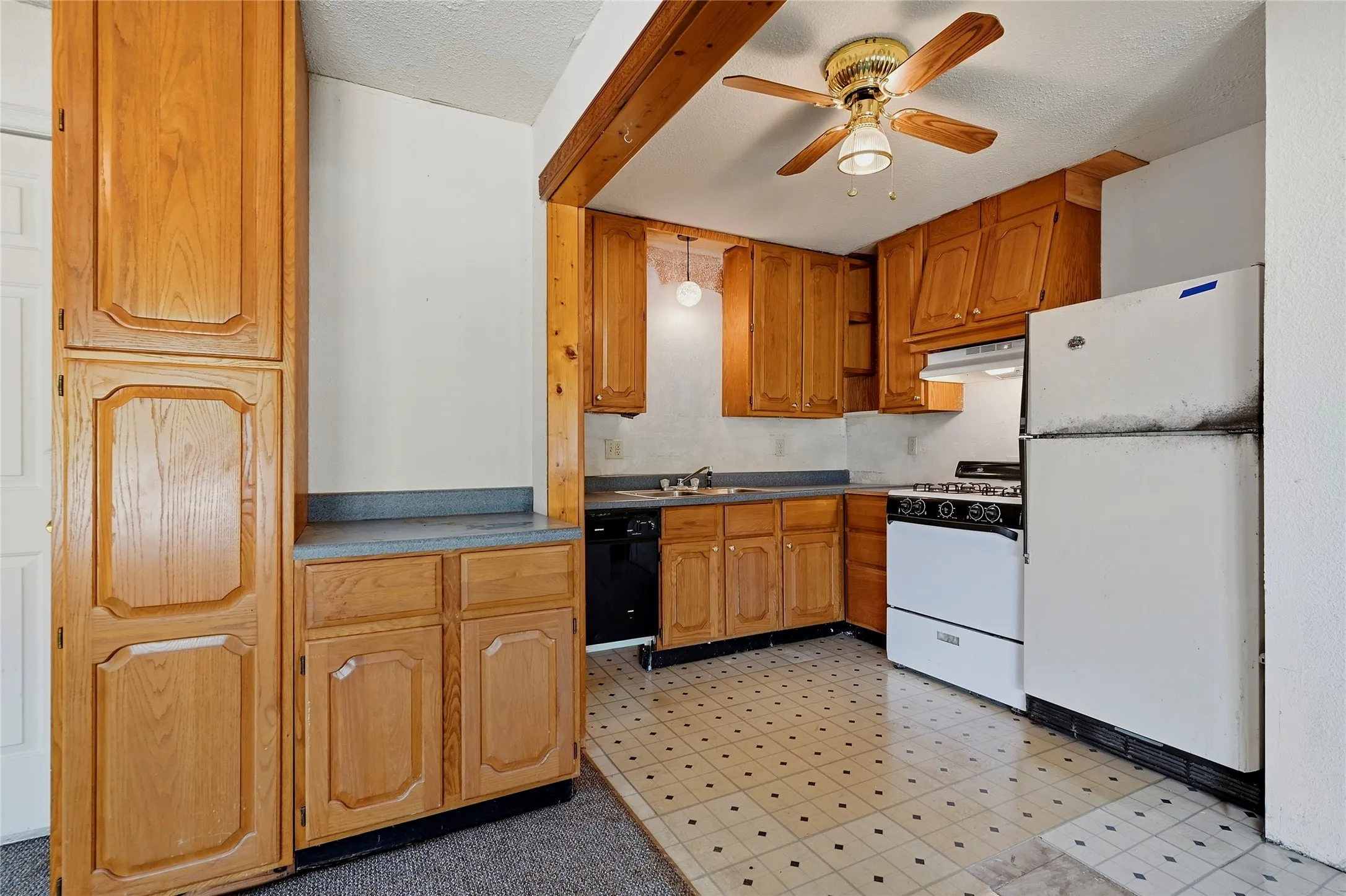 Kitchen featuring wood cabinetry, laminate countertops, a gas range, dishwasher, and patterned tile flooring