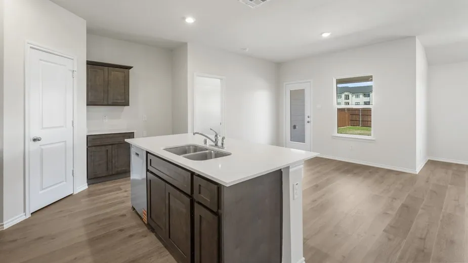 Kitchen island with a dual-basin sink and stainless-steel faucet, white solid surface countertops, wood-finish flooring, and recessed lighting