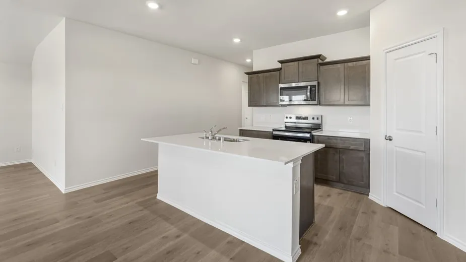 Kitchen island with integrated sink, wood-finish flooring, recessed lighting, stainless steel appliances, and dark wood cabinetry