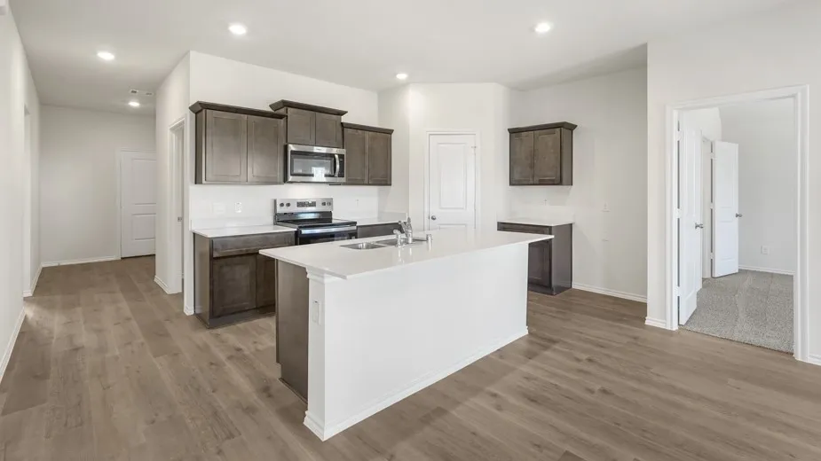 Contemporary kitchen featuring dark wood-finish cabinetry, stainless steel appliances, a white island with an integrated sink, and wood-finish flooring