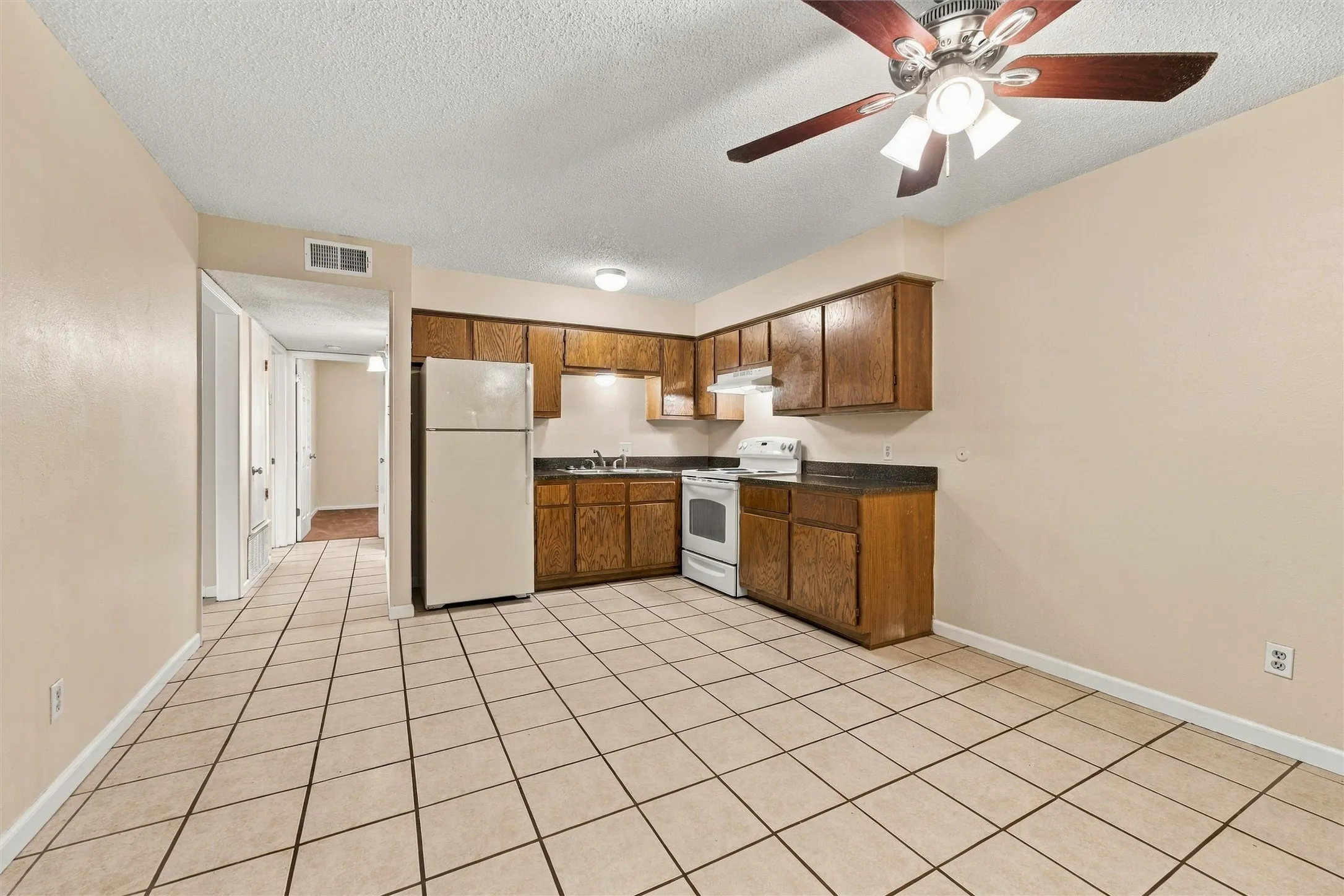 Kitchen area featuring wood-finish cabinetry, white appliances, and a ceiling fan with integrated lighting