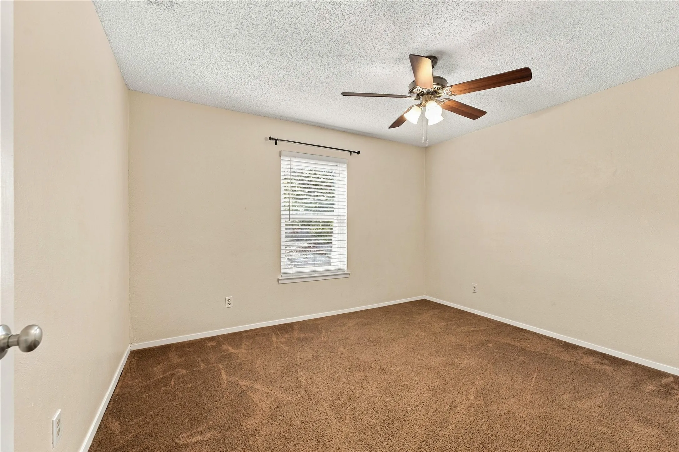 Recessed window with blinds, ceiling fan with light fixture, and brown carpet flooring