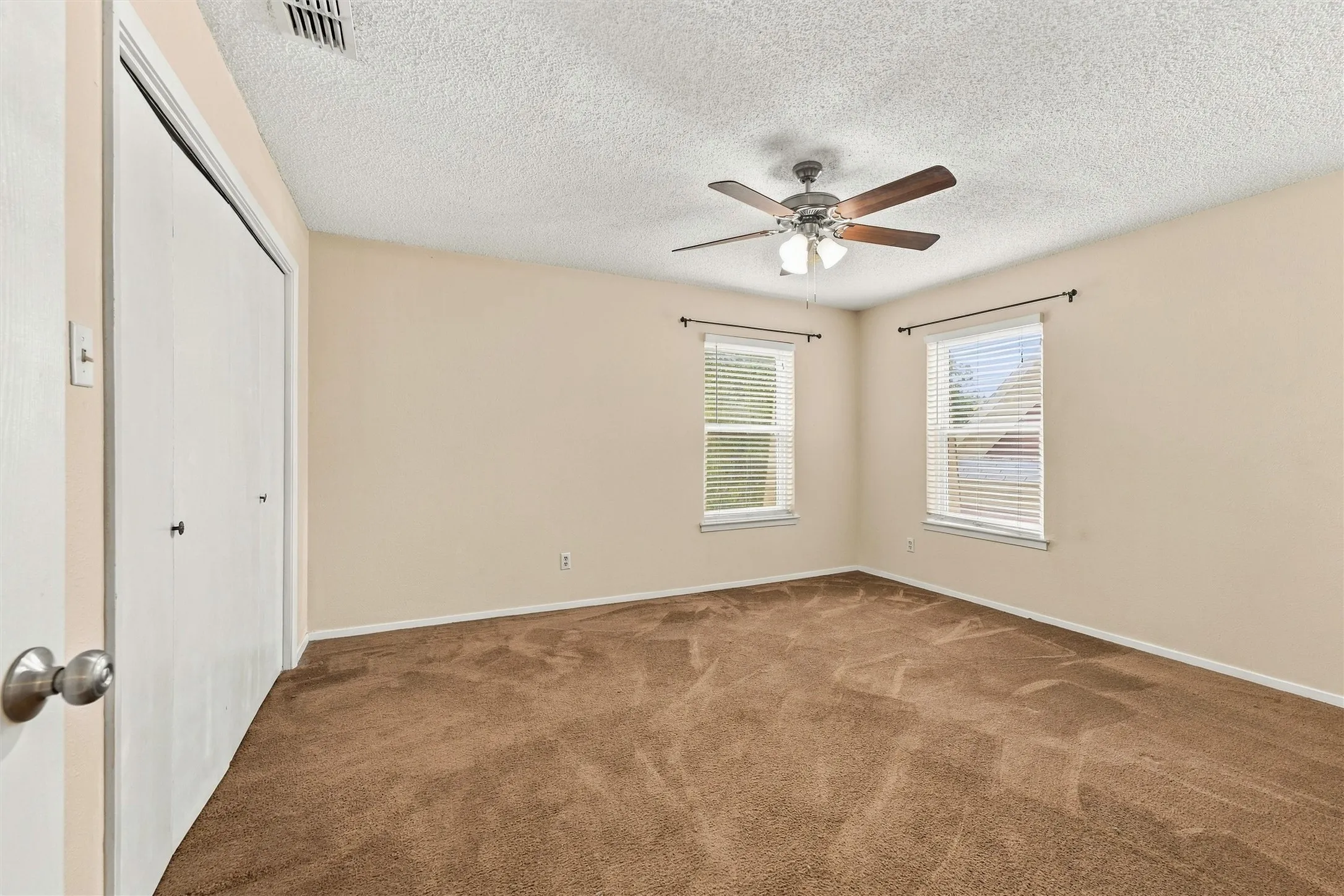 Brown carpeted flooring, two windows with blinds, a ceiling fan with light fixture, and a white bi-fold closet door