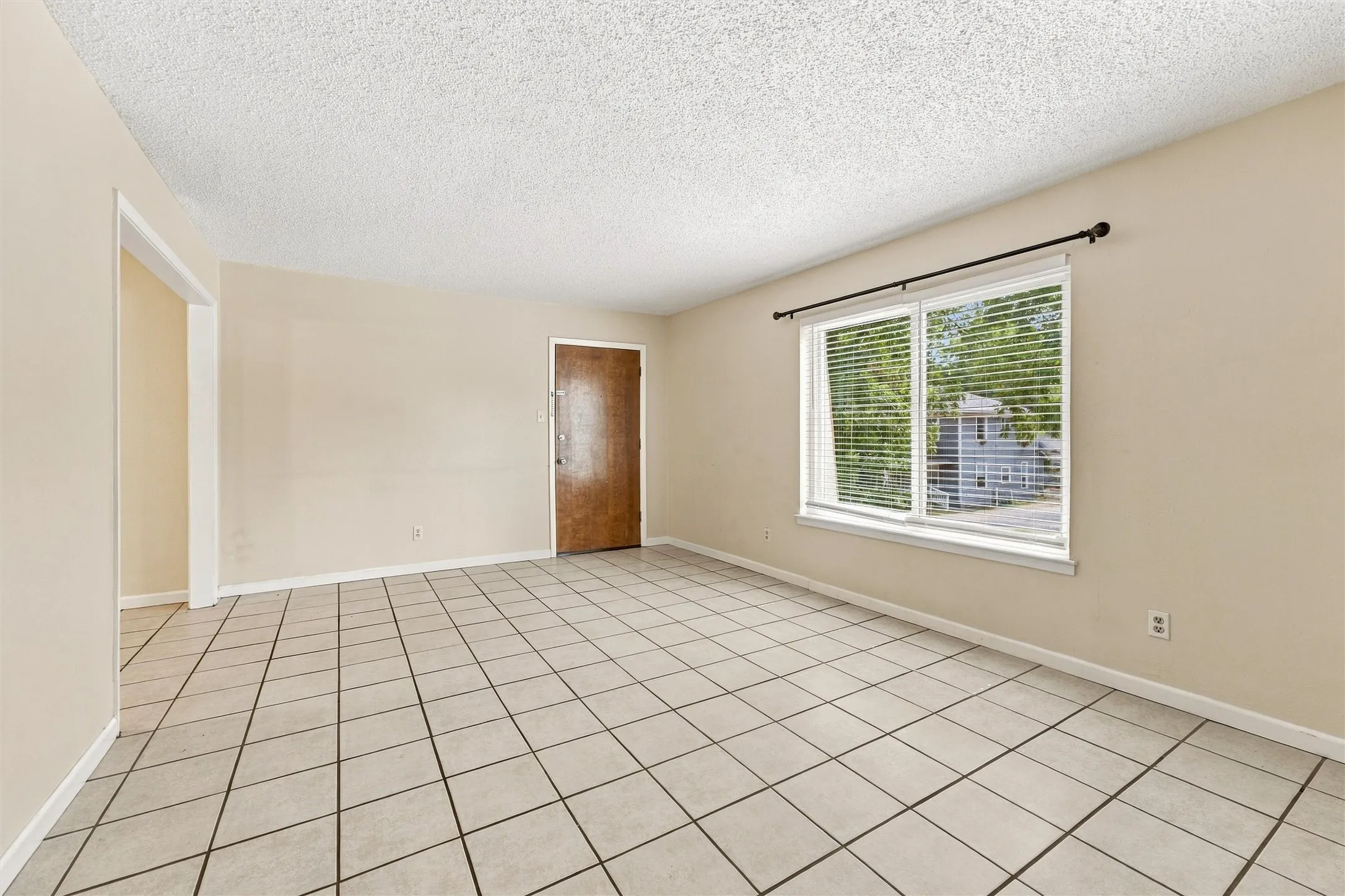 Spacious room featuring tile flooring, neutral wall tones, a large window, and a wood-finish entry door