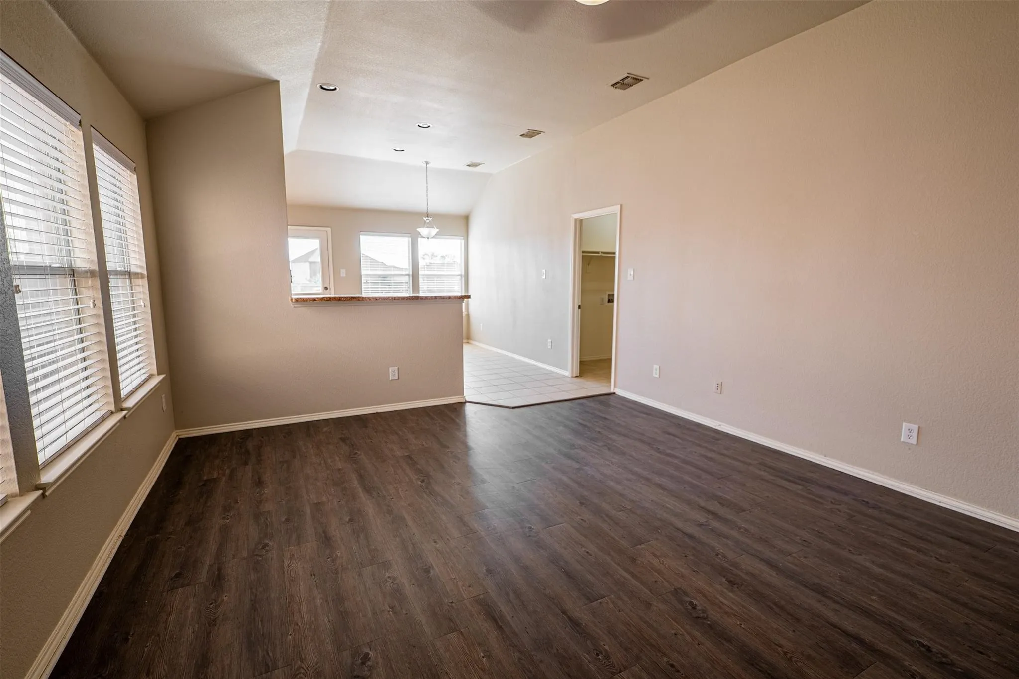 Spacious room with wood-finish flooring, vaulted ceiling, and multiple windows with blinds