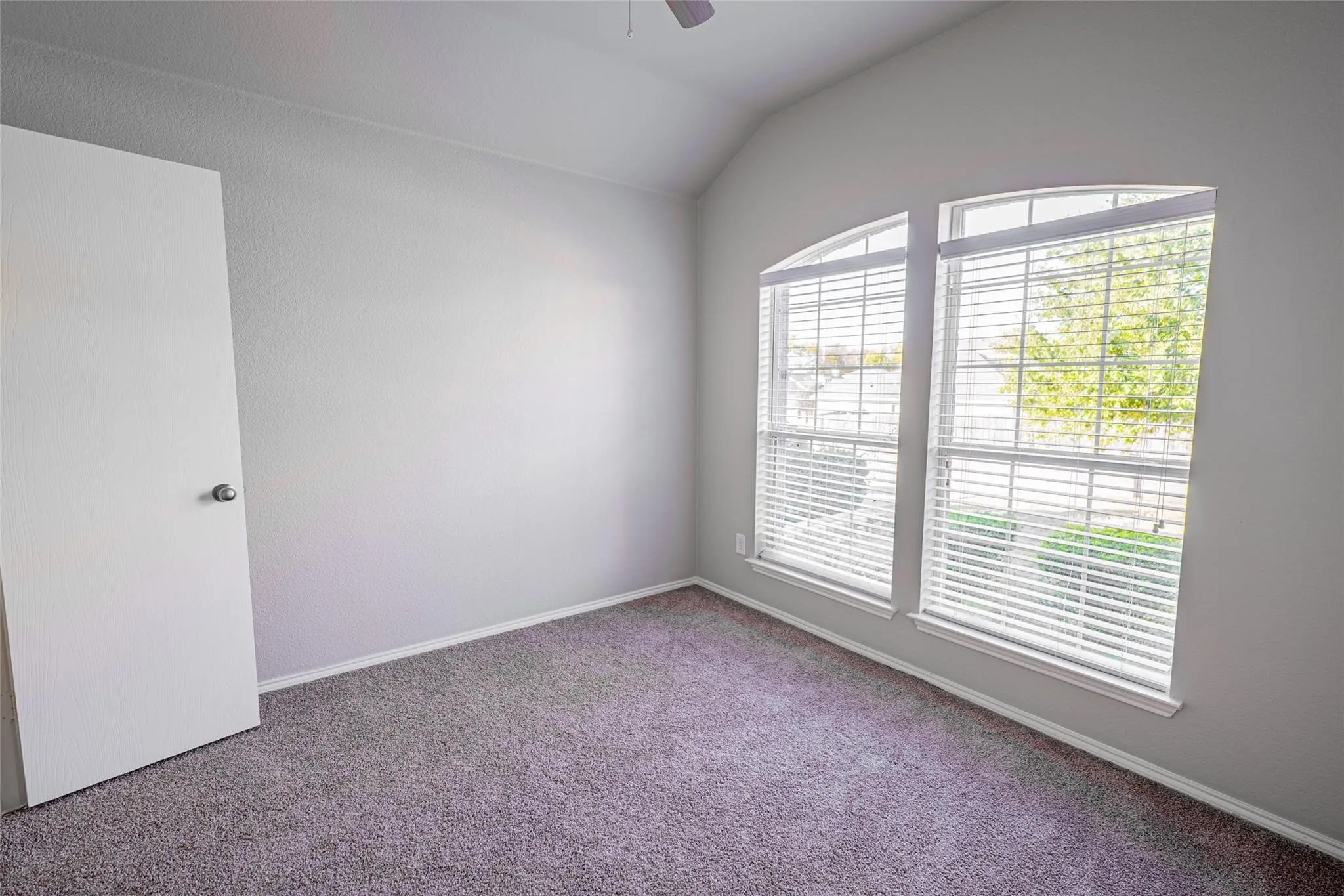 Vaulted ceiling, arched window, carpeted flooring, and neutral wall color