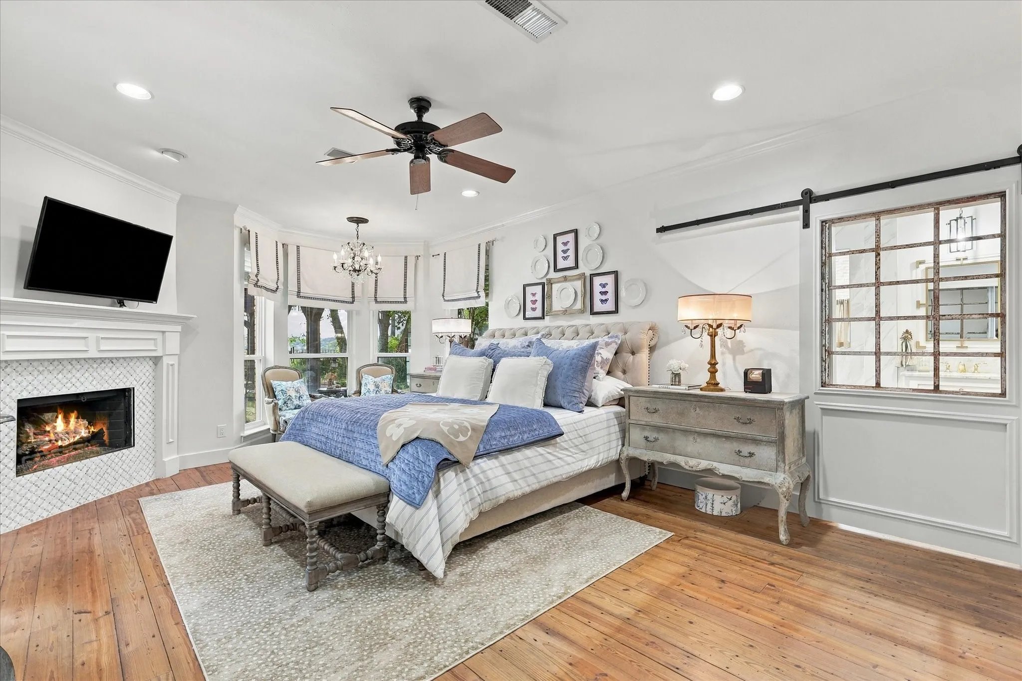 Oversized primary bedroom with so many updated features. Wood floors accent this beautiful space with custom tiled fireplace, sitting area with designer window treatments and barn door leading to bathroom area.
