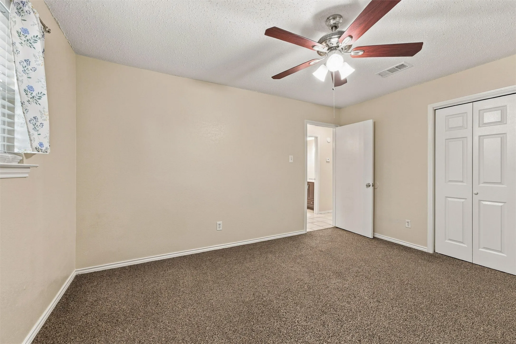 Textured carpet flooring, neutral-toned walls, and a ceiling fan with integrated lighting