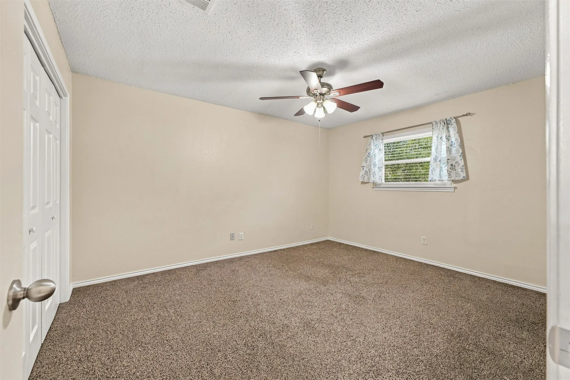 Neutral wall finishes, textured ceiling, ceiling fan with integrated lighting, carpeted flooring, and a single window