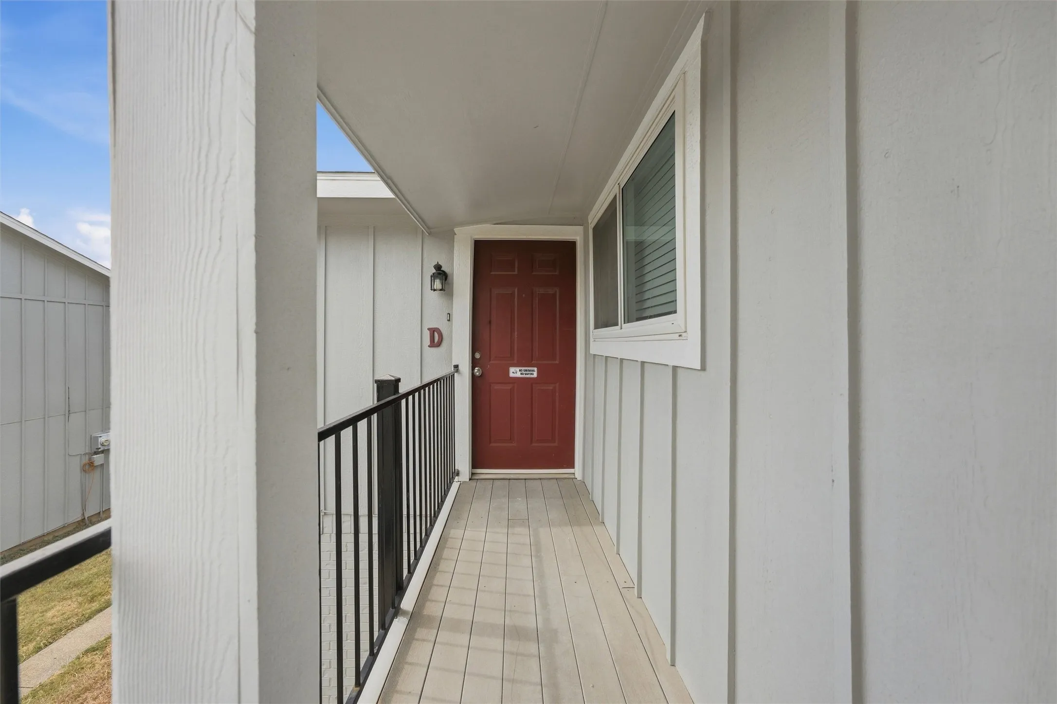 Covered porch entry featuring a red door, exterior lighting, window with blinds, and white siding