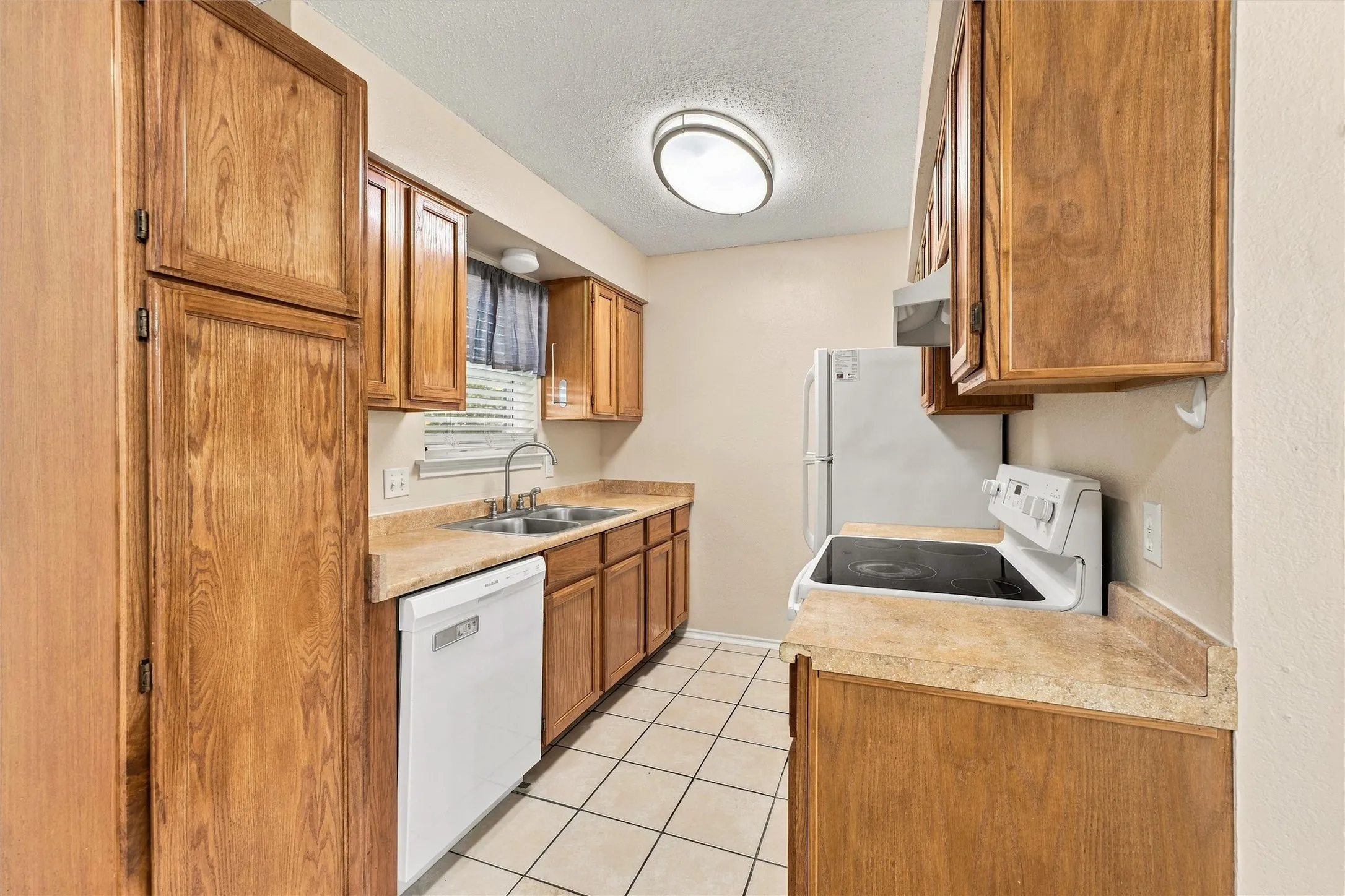 Galley kitchen with wood-finish cabinetry, tile flooring, and laminate countertops