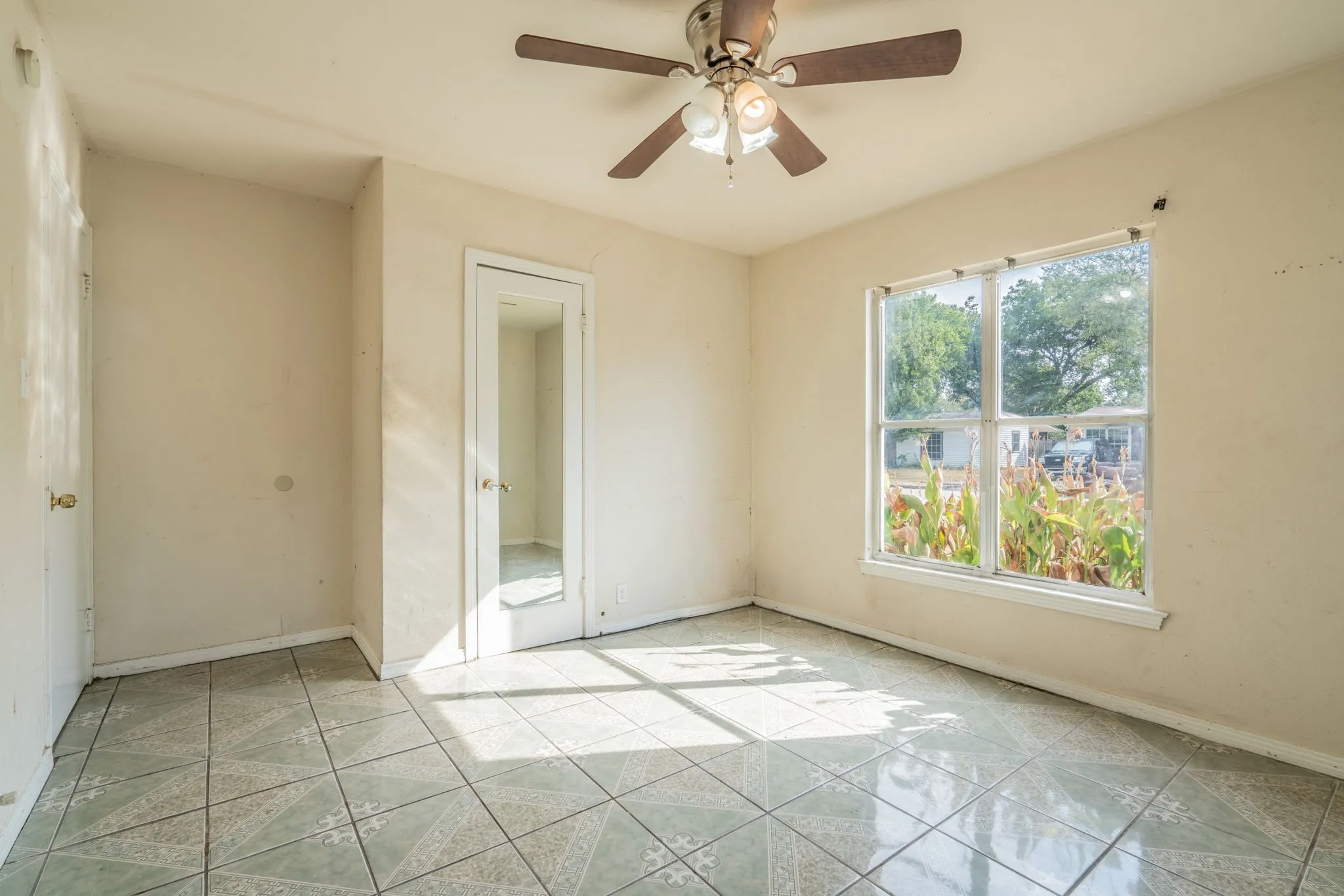 Ceramic tile flooring, ceiling fan with integrated lighting, and a large window providing ample natural illumination