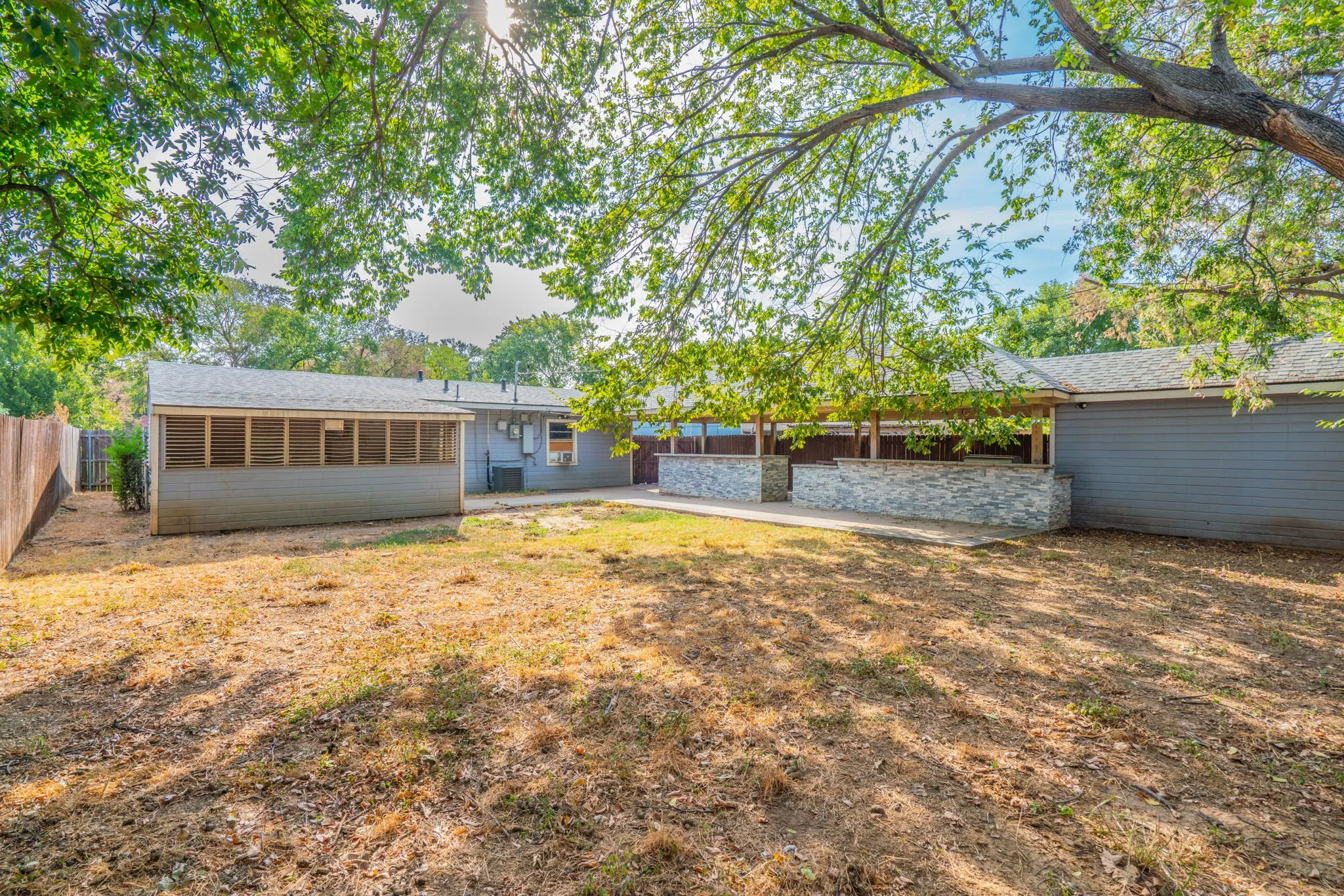 Expansive backyard featuring a screened-in porch, mature trees, and a stone-clad patio area