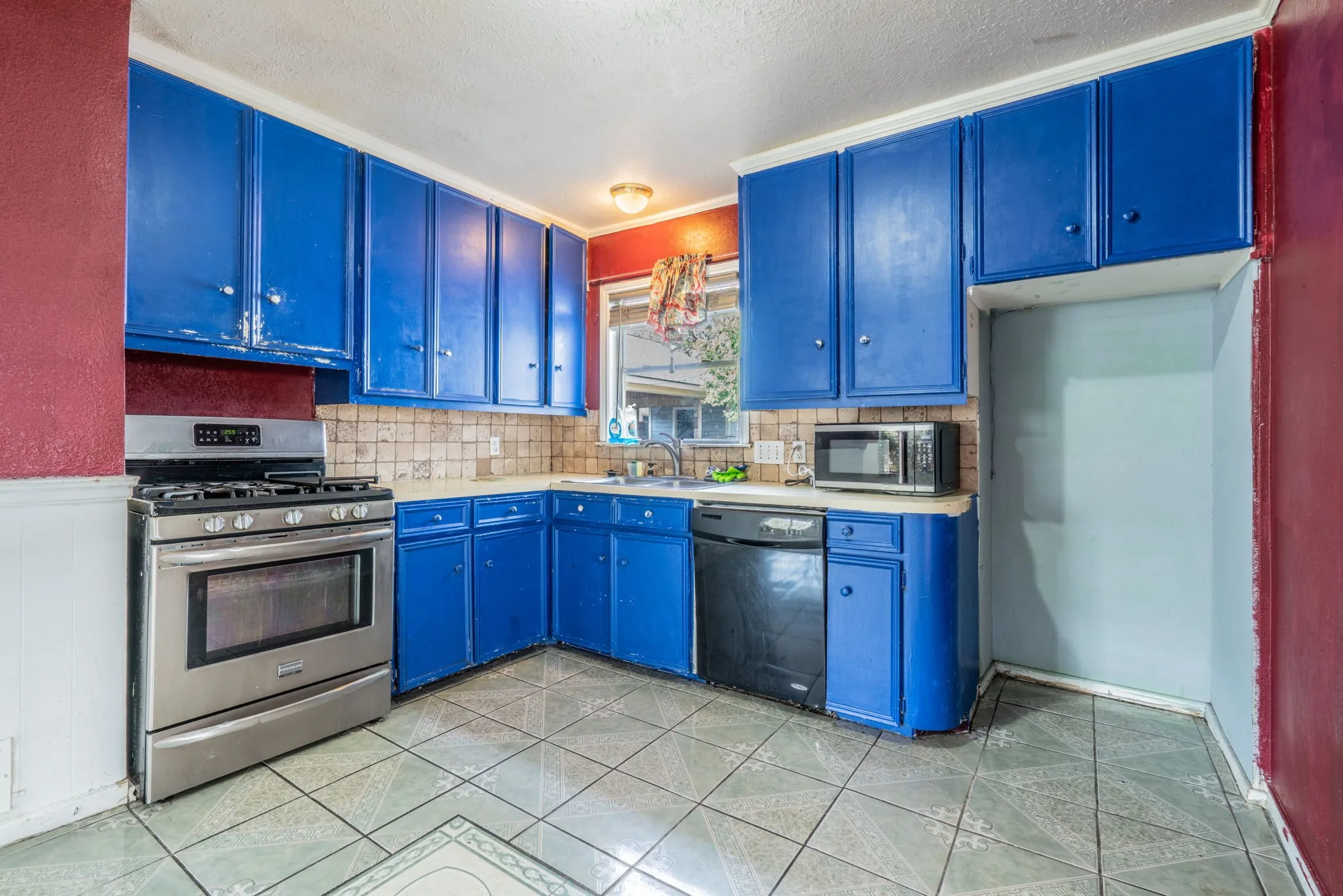 Stainless steel range, tile backsplash, built-in dishwasher, and a window above the sink