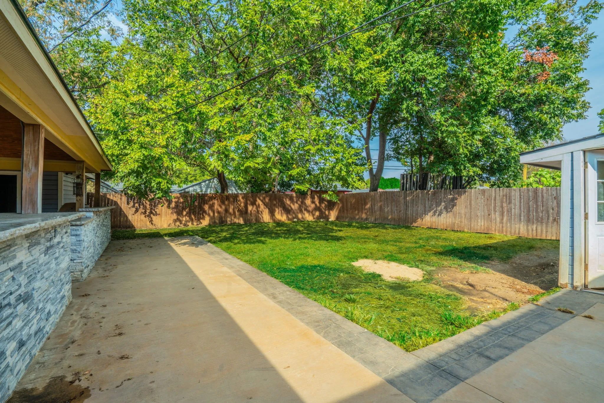 Expansive backyard featuring a manicured lawn, established trees, wood fencing, and a concrete patio