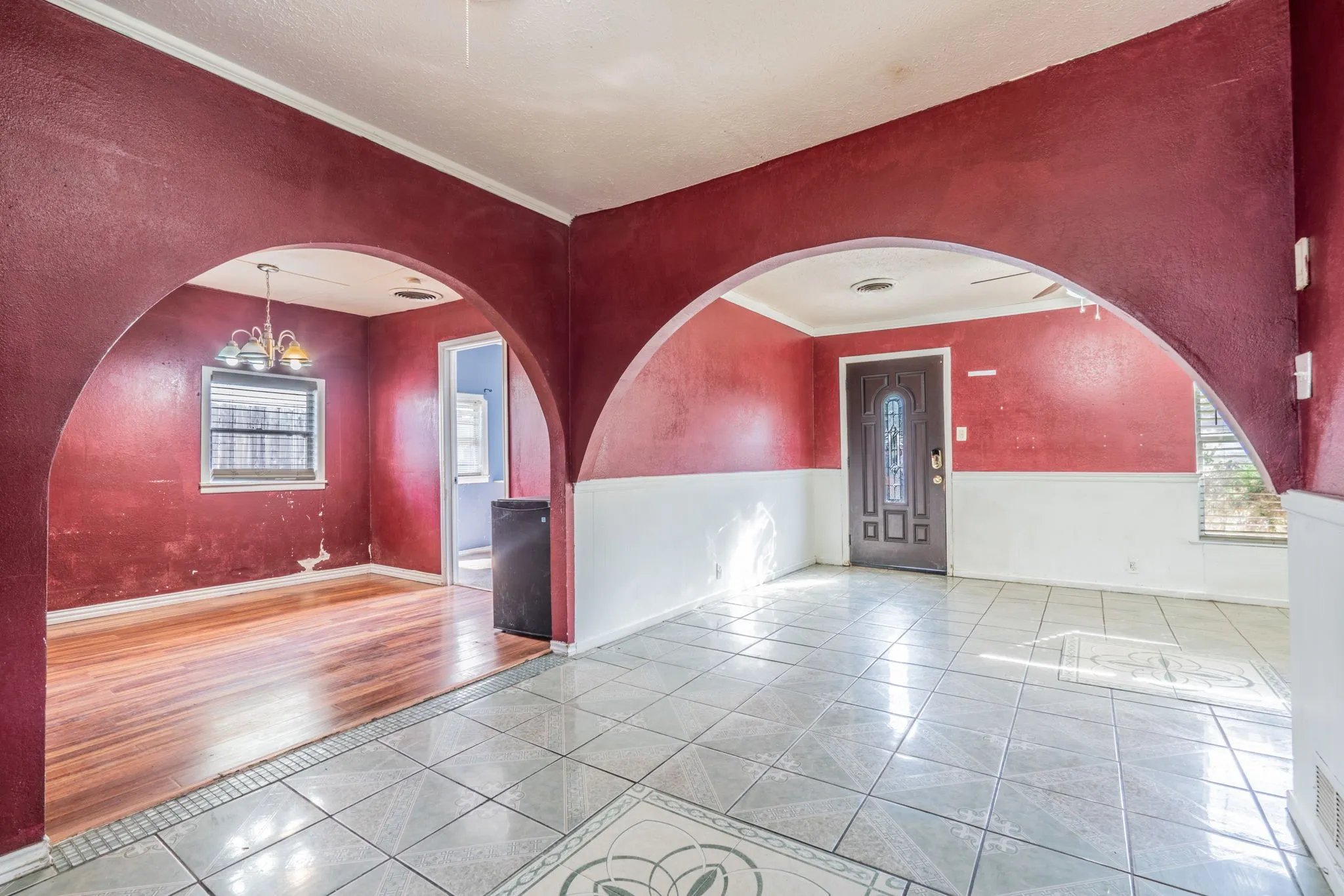Arched doorways frame distinct living spaces, featuring tile flooring in one area and wood-finish flooring in another