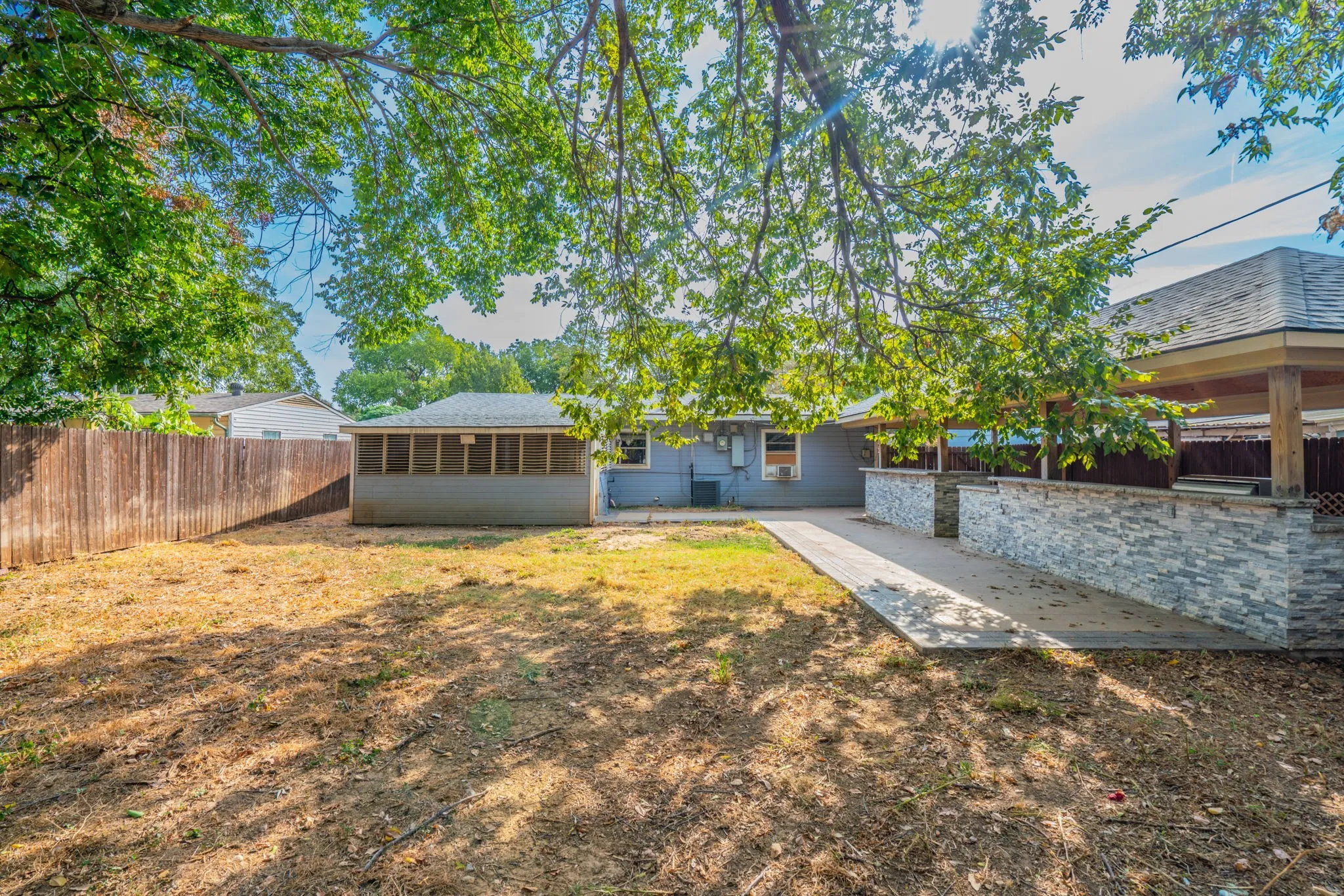 Expansive backyard featuring a privacy fence, covered patio with stone-veneer knee walls, and a screened-in porch