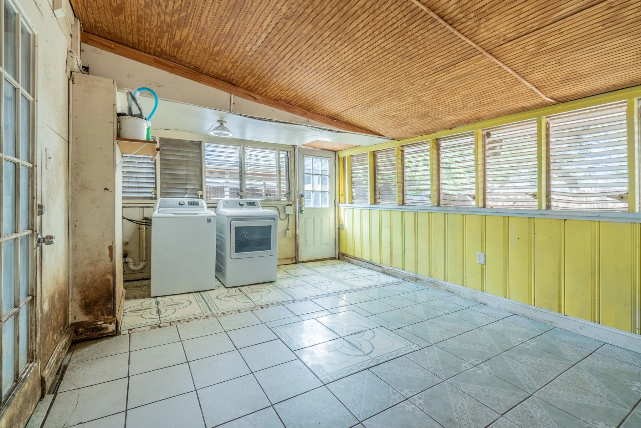 Tile flooring, wood-paneled ceiling, multiple window openings, and a utility sink
