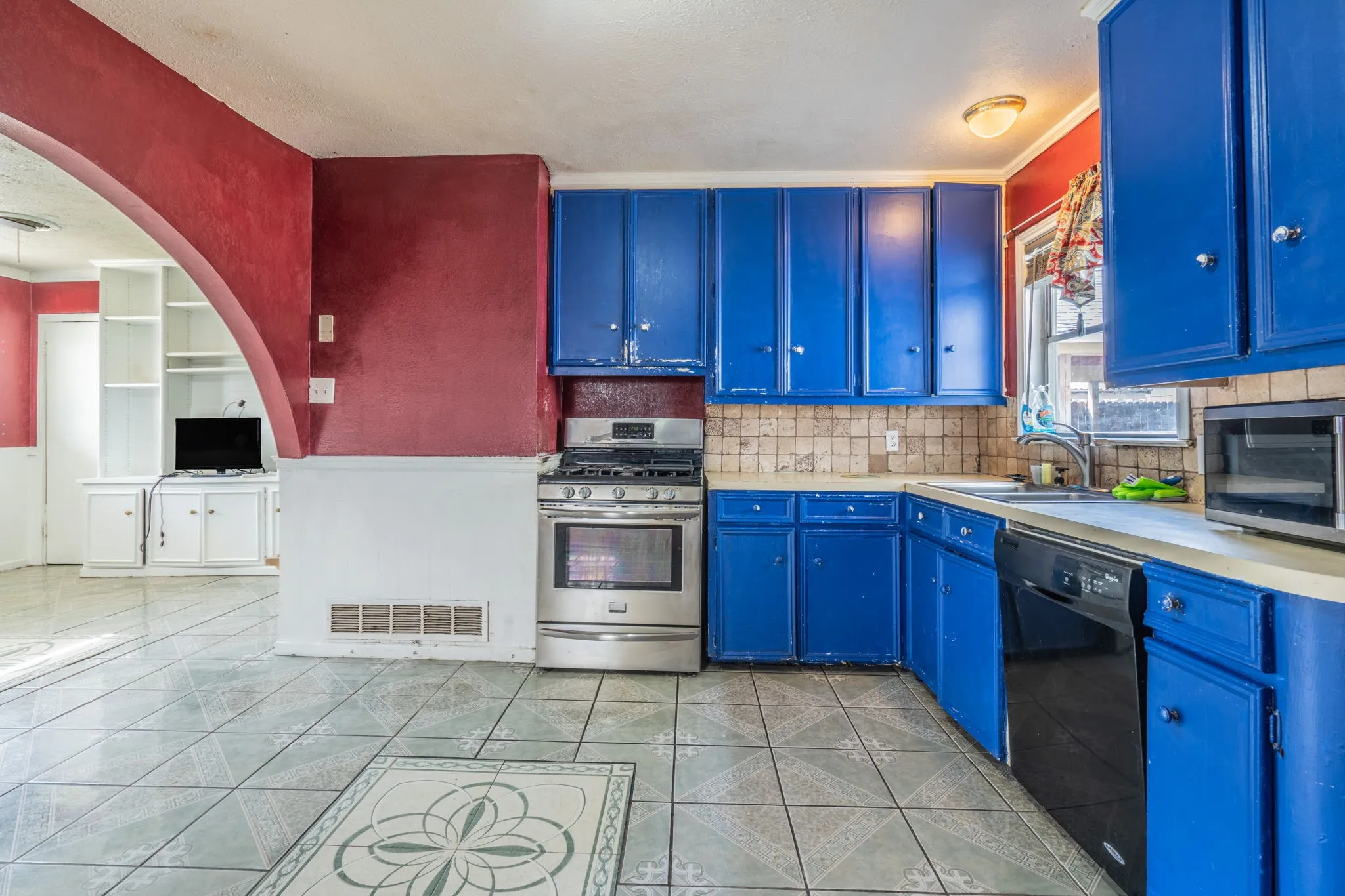 Kitchen featuring blue cabinetry, tile backsplash, built-in dishwasher, and stainless steel gas range