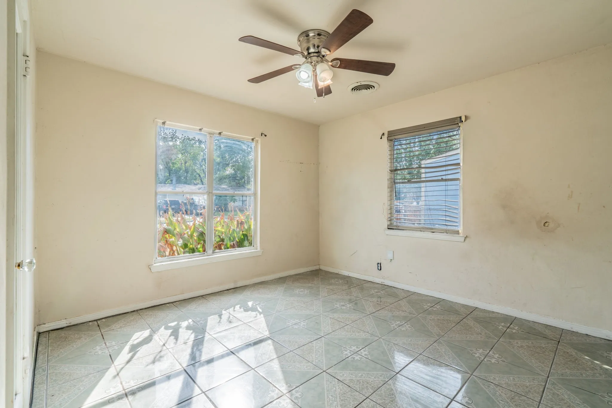 Patterned tile flooring, ceiling fan with integrated lighting, two windows with blinds, and painted walls
