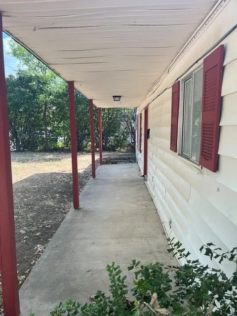 Covered front porch with a concrete walkway, red support pillars, and a mounted exterior light fixture