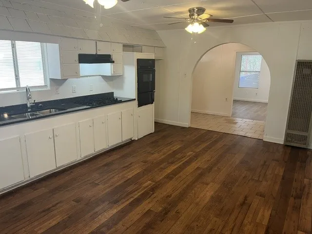 Kitchen with wood-finish flooring, white cabinetry, dark countertops, and stainless steel sink