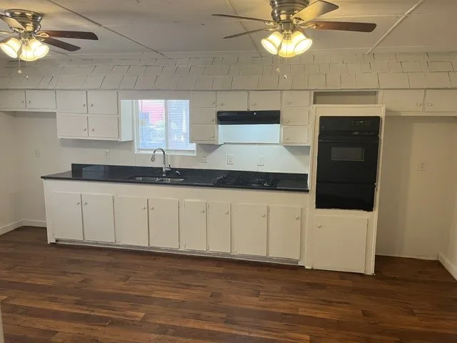 Kitchen featuring white cabinetry, dark countertops, a built-in oven, and wood-finish flooring