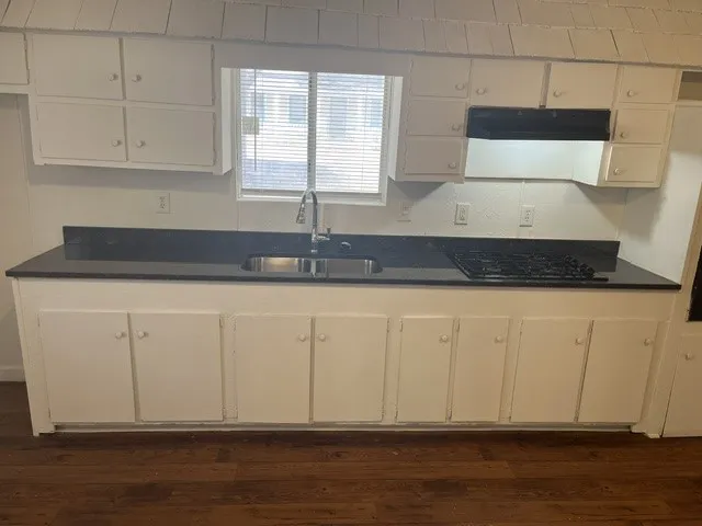 Kitchen featuring white cabinetry, dark countertops, a stainless steel sink with a gooseneck faucet, a built-in gas cooktop, and wood-finish flooring