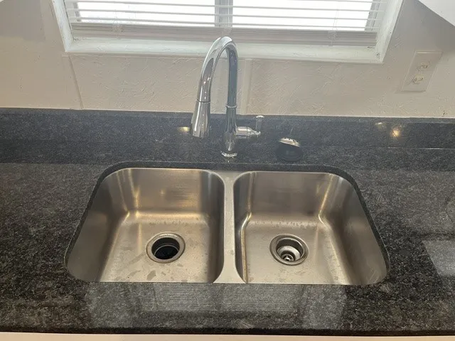 Dual basin stainless steel sink with a high-arc chrome faucet, set into a dark speckled countertop