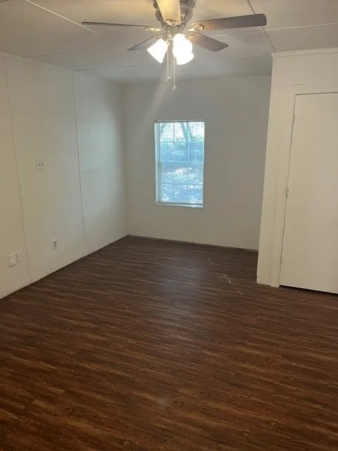 Wood-finish flooring, white paneled walls, ceiling fan with integrated lighting, and a single window