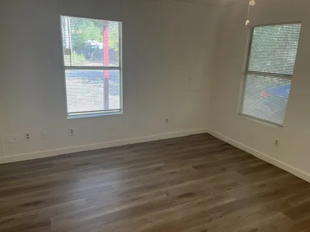 Wood-finish flooring, white painted walls, and two windows with blinds