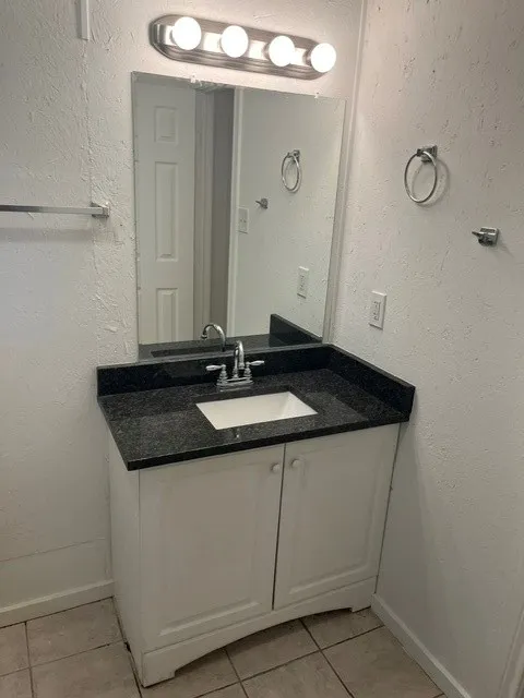 White vanity with a dark countertop, an undermount sink, and a chrome faucet