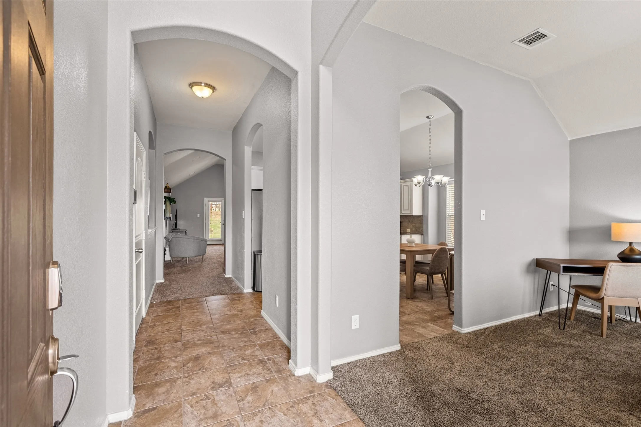 Arched doorways, vaulted ceiling, tile flooring, brown carpet, and a wooden entry door