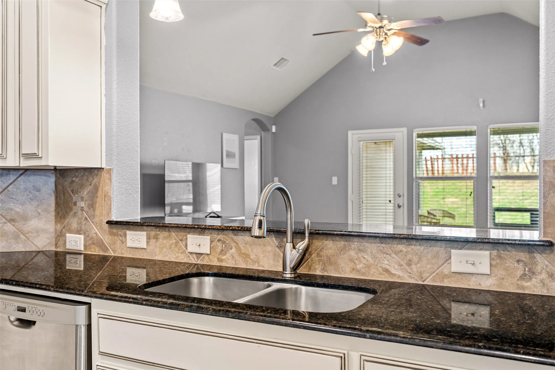 Kitchen featuring dark countertop, stainless steel double basin sink with a high-arc faucet, and tiled backsplash