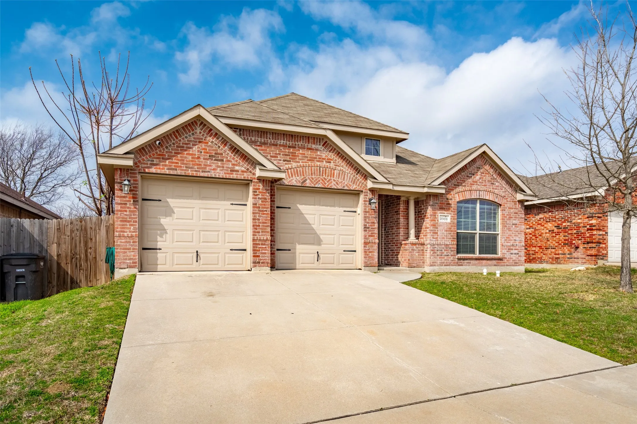 Brick exterior featuring a two-car garage, concrete driveway, and covered entry