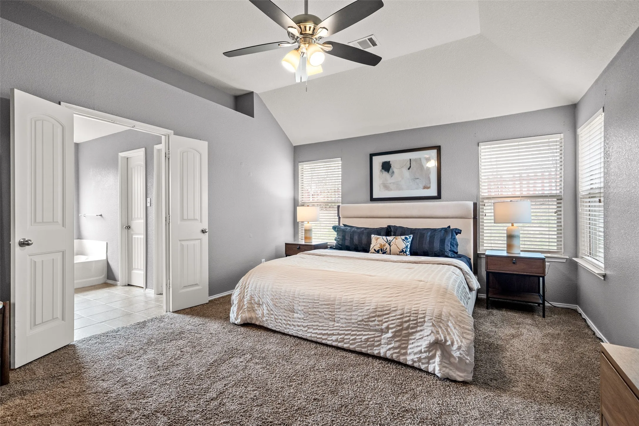 Vaulted ceiling with a ceiling fan, carpet flooring, dual windows with blinds, and white double doors