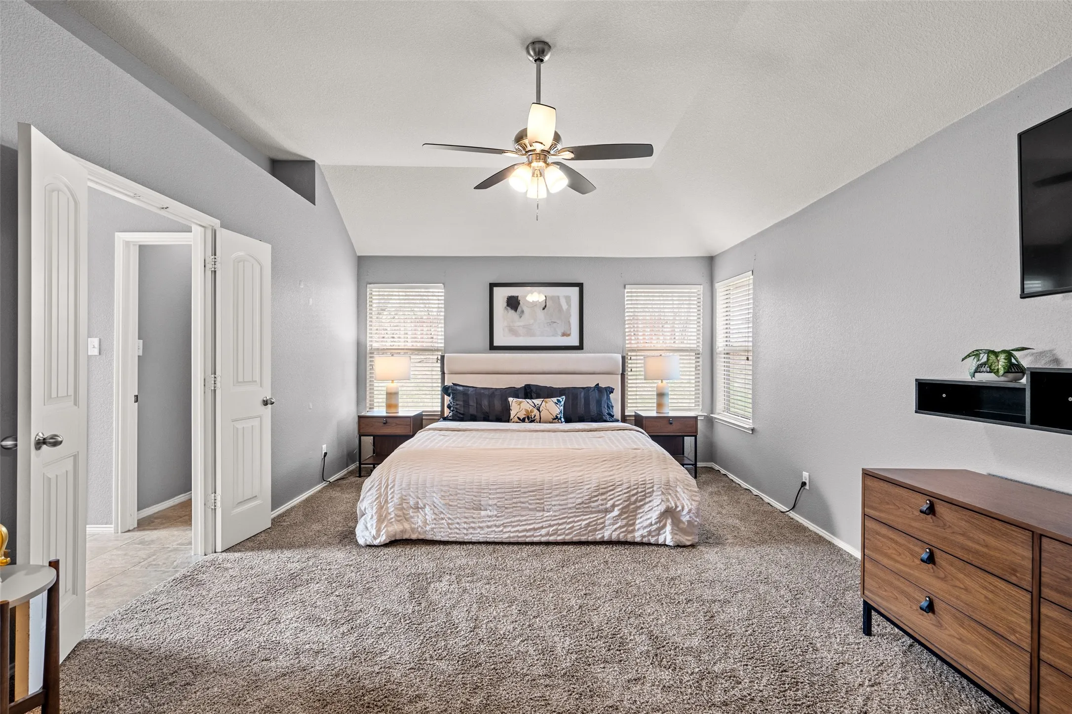 Vaulted ceiling with ceiling fan, two windows with blinds, carpet flooring, and white interior doors