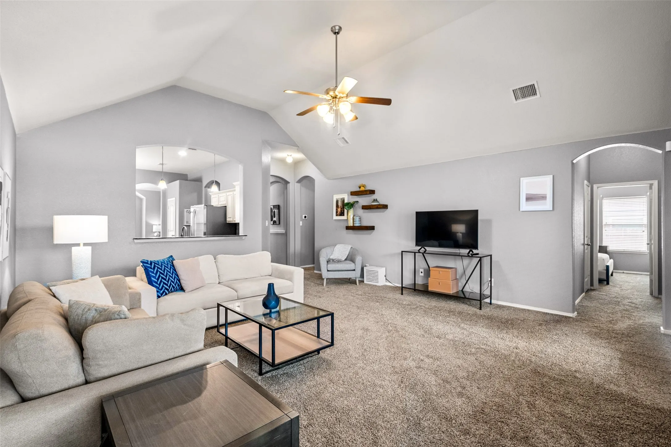 Vaulted ceiling with ceiling fan, recessed wall archway, pass-through window, and built-in floating shelves