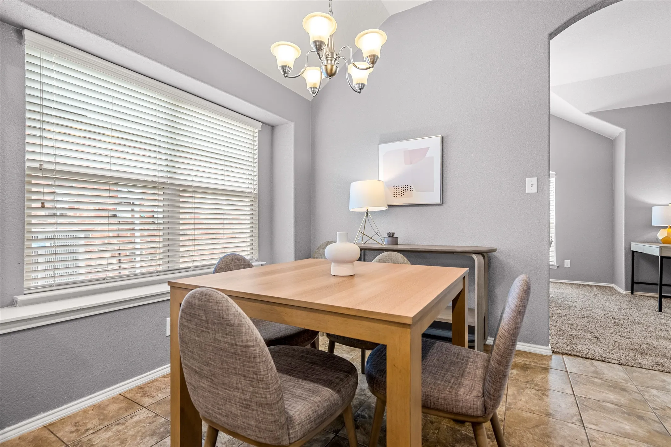 Recessed window with blinds, tile flooring, arched doorway, and overhead chandelier