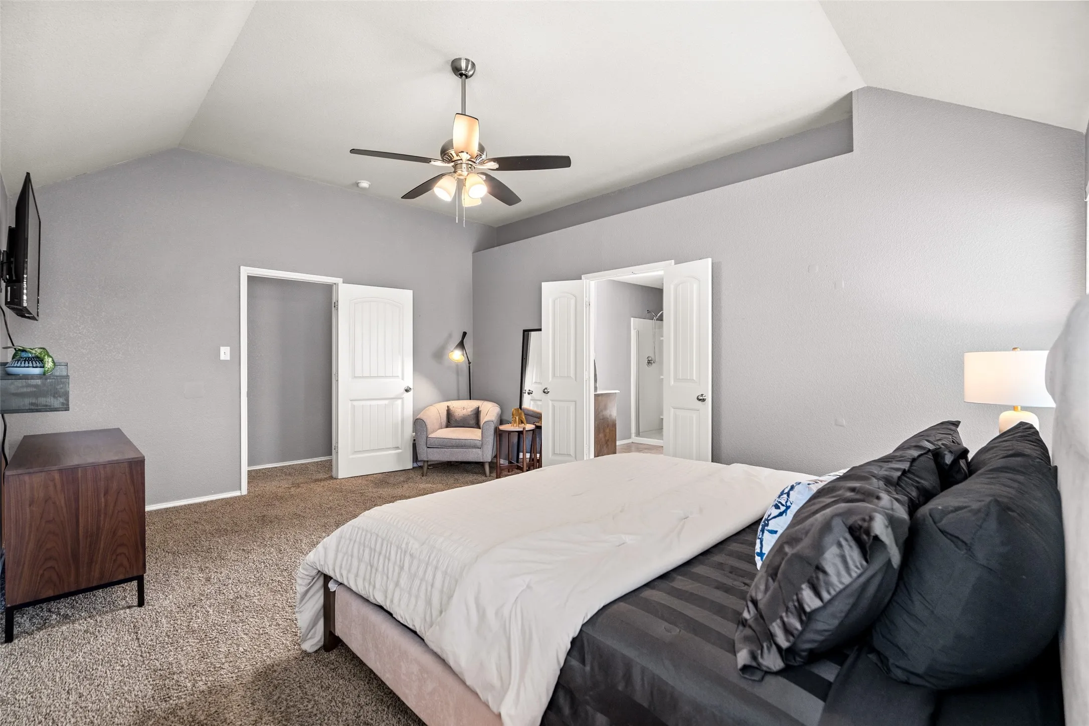 Vaulted ceiling with ceiling fan, dual white panel doors, and neutral wall tones