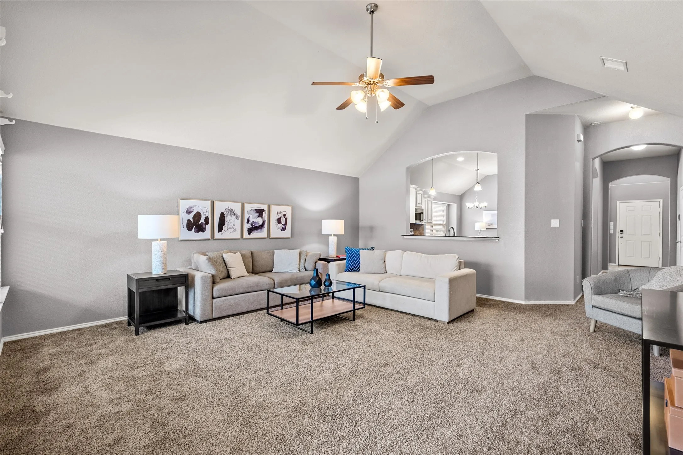 Vaulted ceiling with an attached ceiling fan, carpeted flooring, and a pass-through window with a built-in countertop
