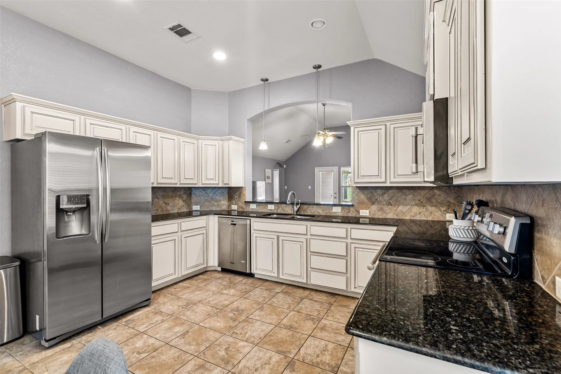 Kitchen featuring tile flooring, white cabinetry, dark stone countertops, stainless steel appliances, and vaulted ceilings
