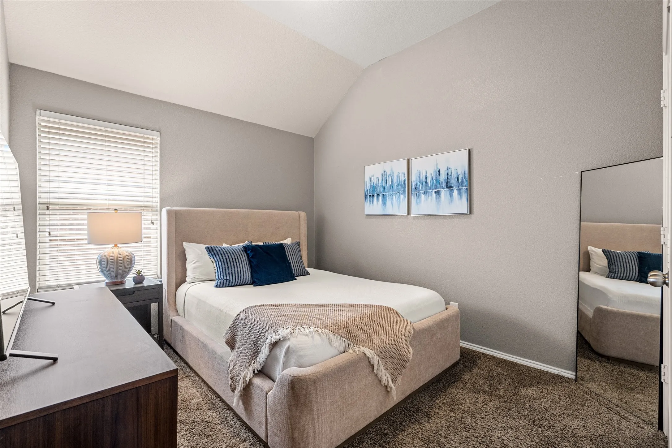 Vaulted ceiling with an angled design, window with blinds, and neutral wall paint