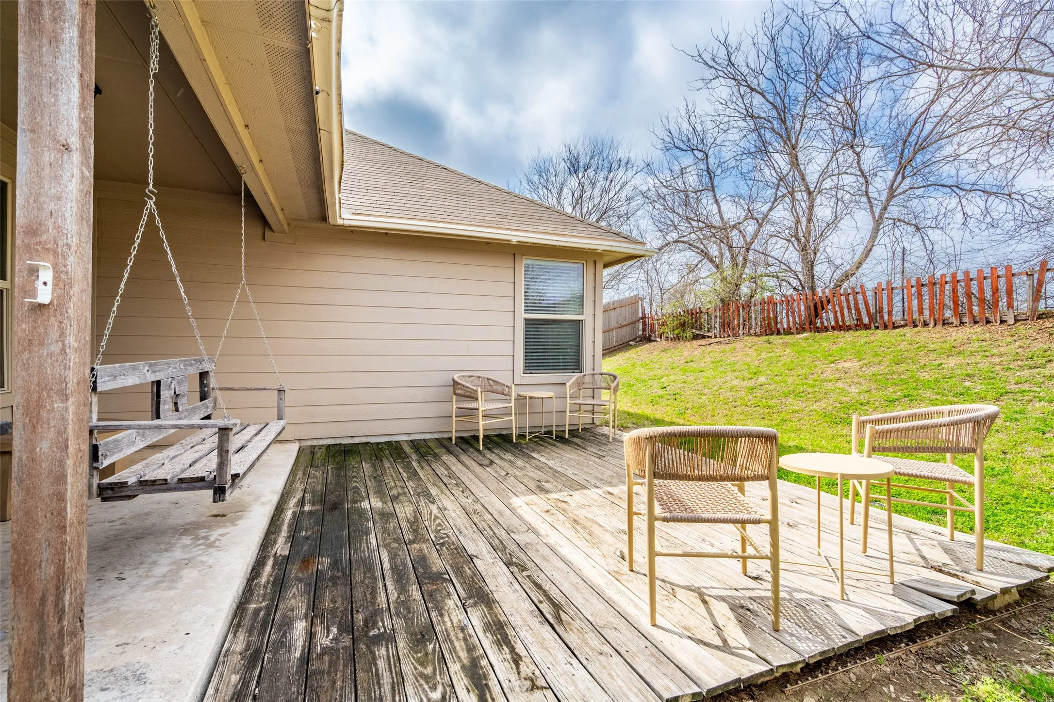 Rear exterior with wood siding, a wooden deck, and a sloped grassy yard with perimeter fencing