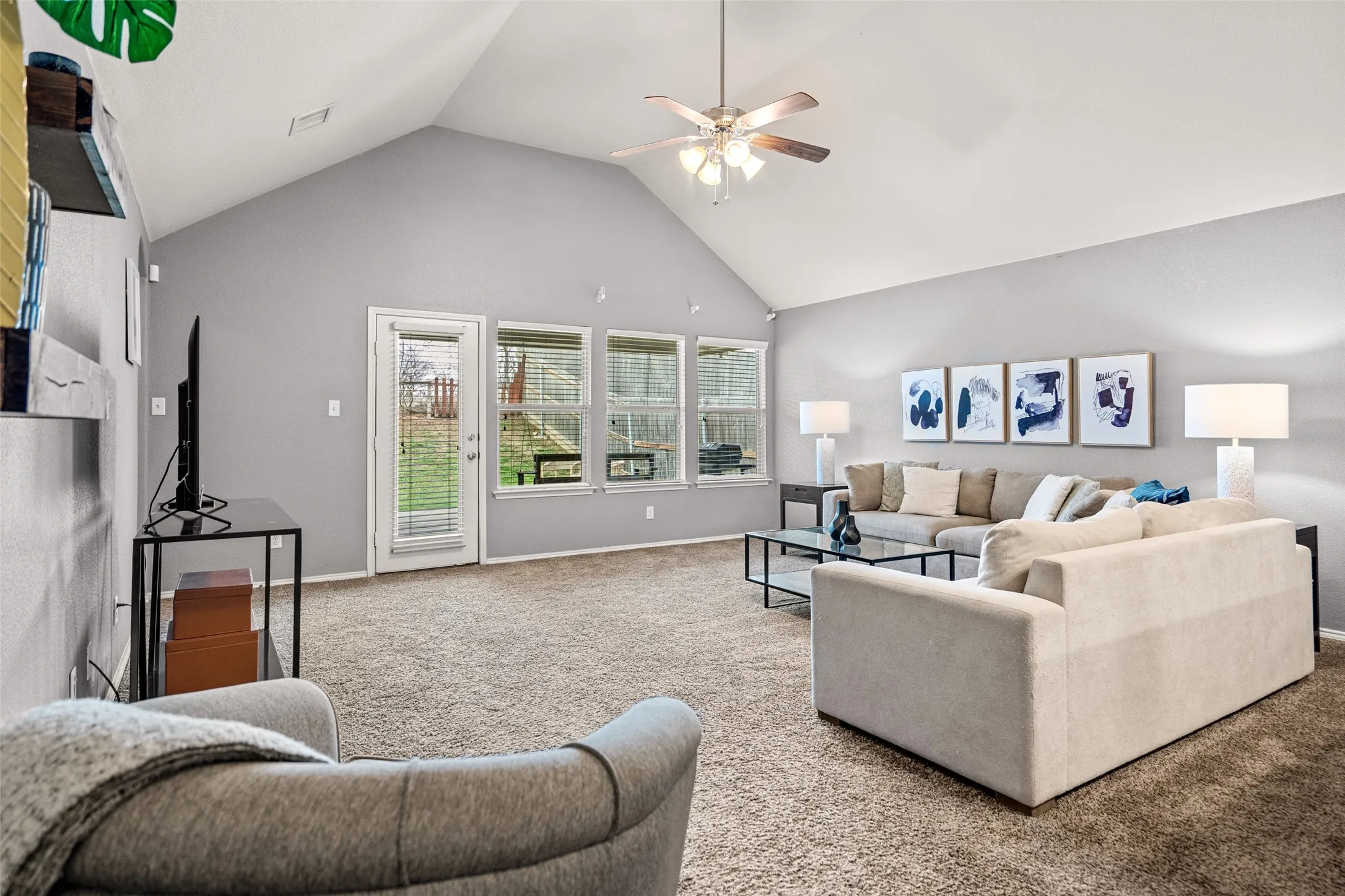 Vaulted ceiling, ceiling fan, carpet flooring, multiple windows, and a glass-paneled door