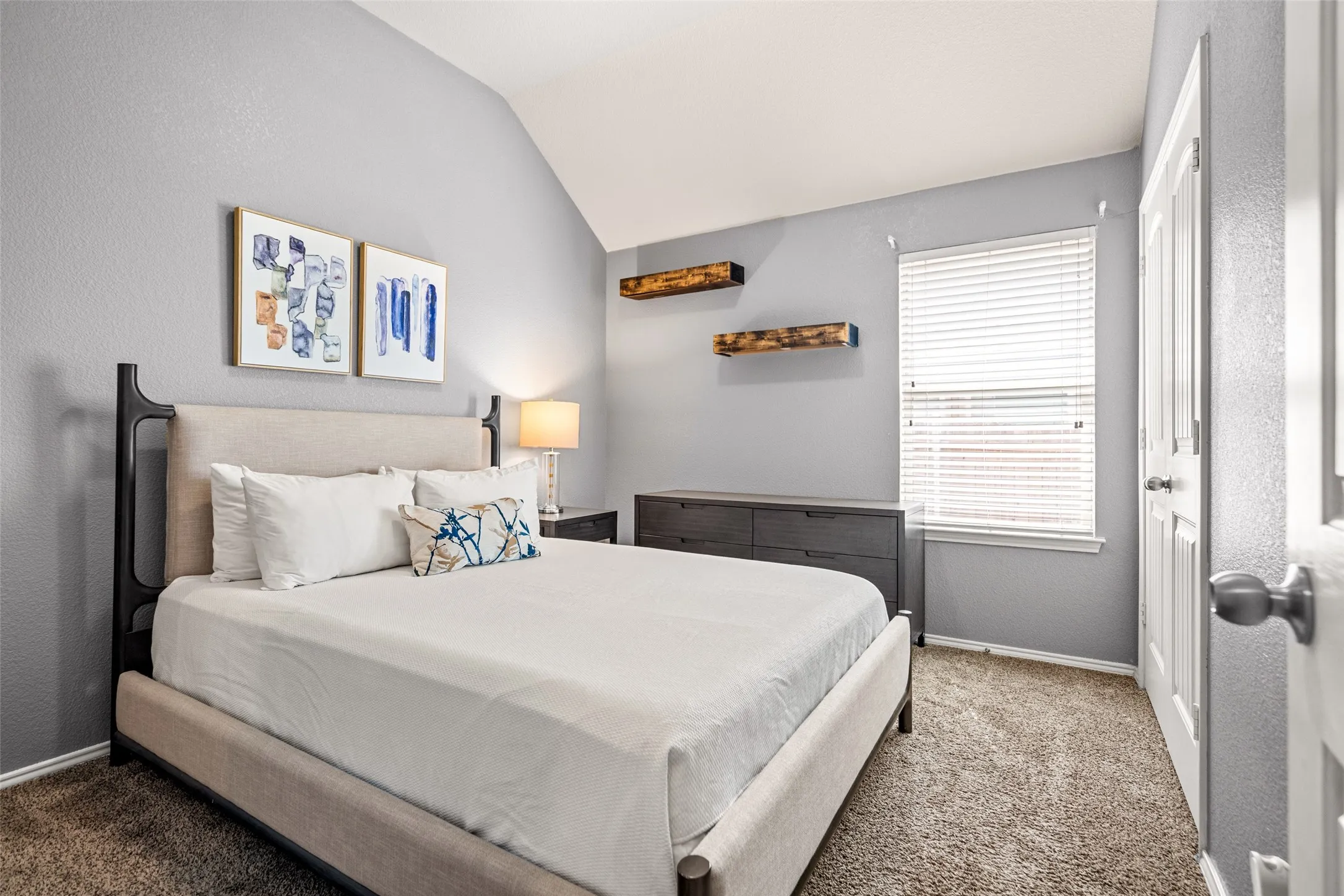 Vaulted ceiling, window with blinds, permanent shelving, built-in closet, and neutral wall tones