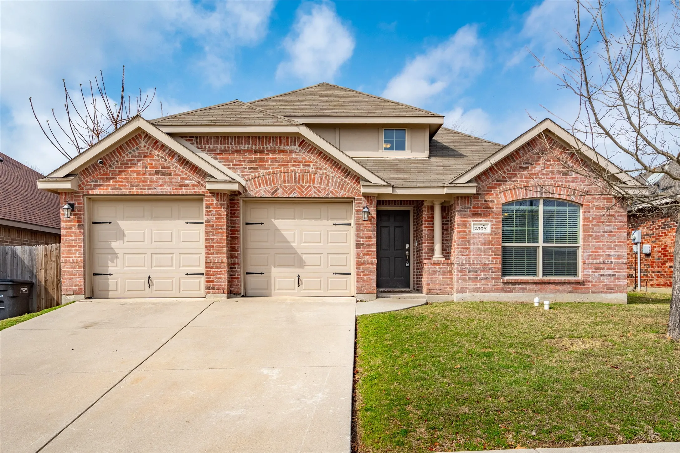 Brick exterior with arched window detailing, two-car garage, concrete driveway, and front entry with a covered porch